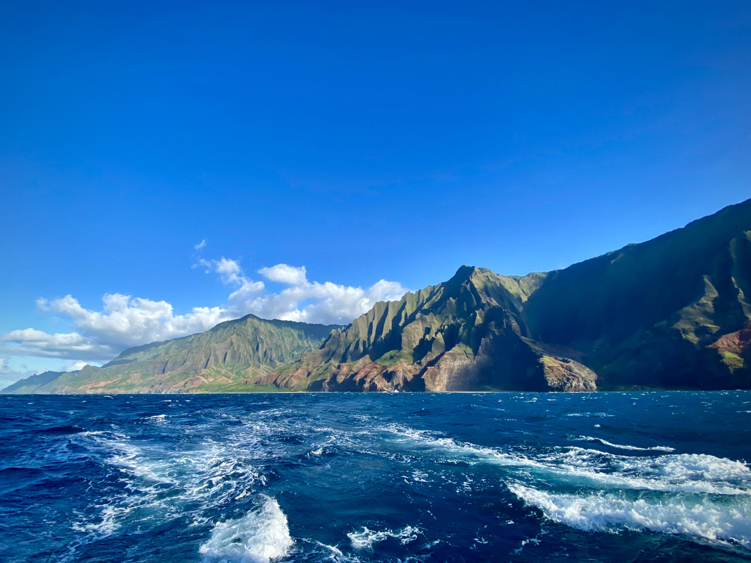 A boat travels across a blue ocean, with mountains in the distance.