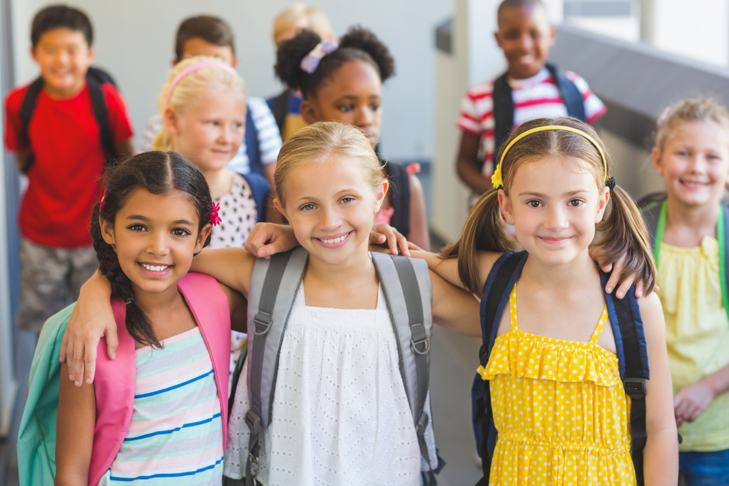 A group of diverse children smile, some wearing backpacks.