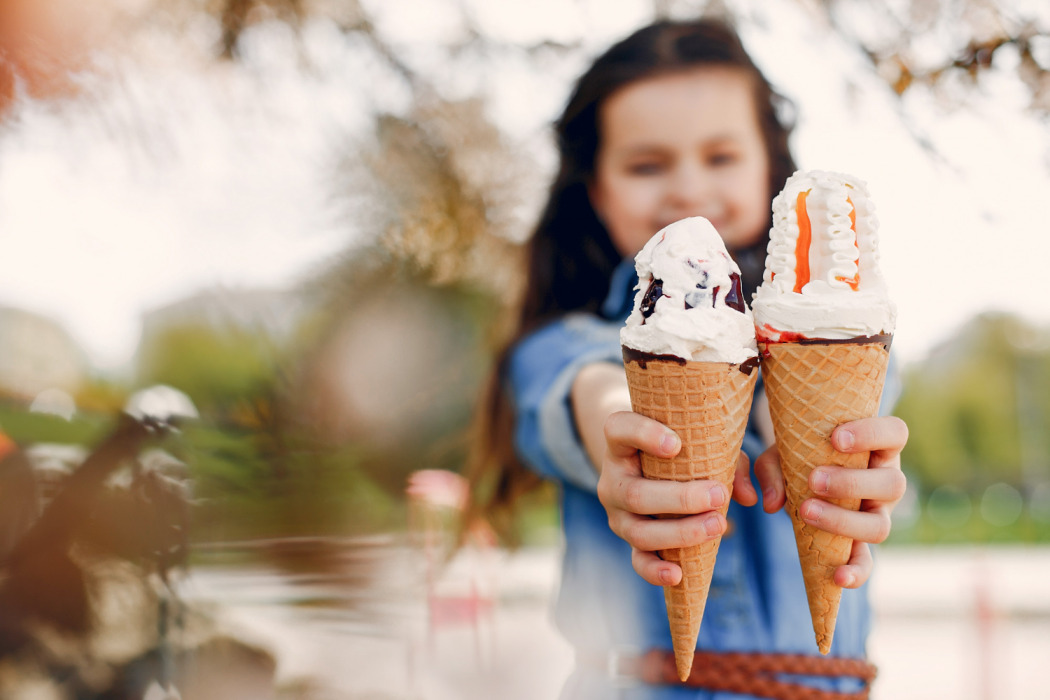 A young person holds out two ice cream cones, smiling at the camera.