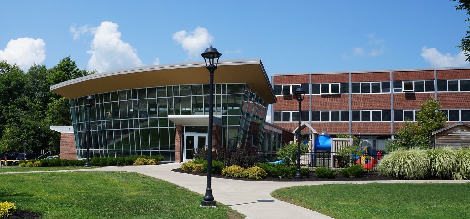 A modern building with large windows and a walkway leading to a playground.