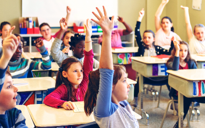 Students in a classroom raise their hands, eager to participate.