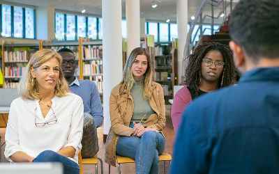 A diverse group of people listens attentively in a library setting.