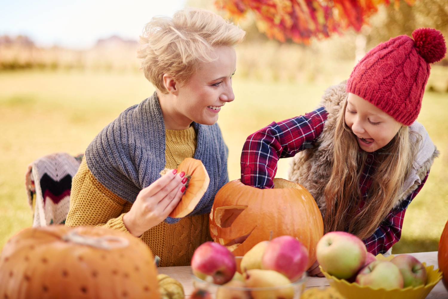 Two children examine pumpkins in a field on a sunny day.