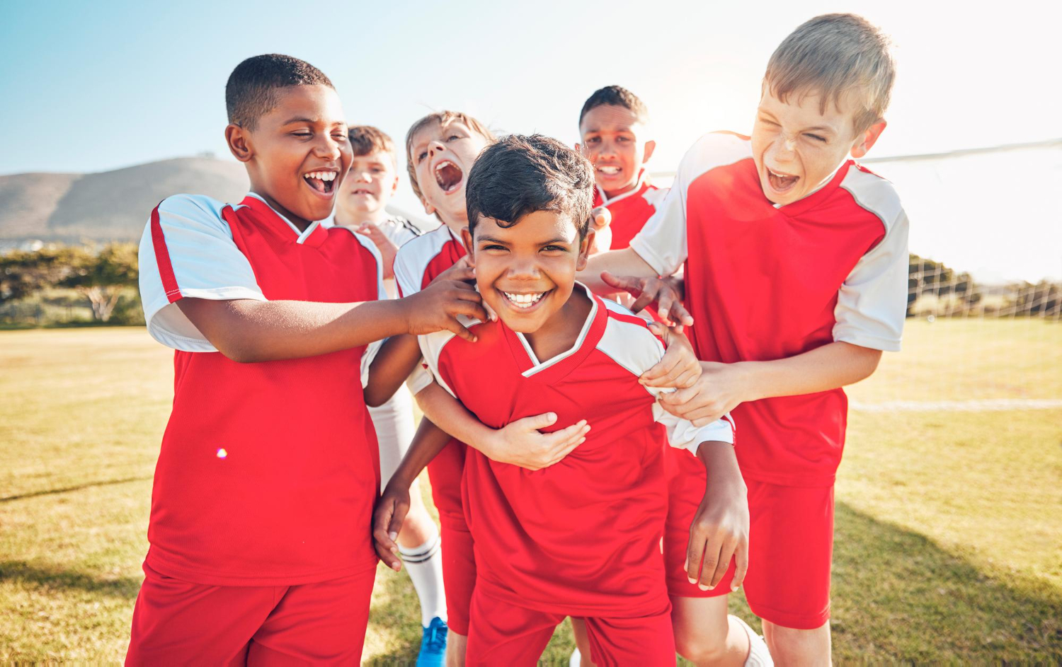 A youth soccer team poses for a photo on a sunny field.