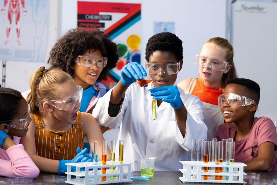 A group of students in safety glasses conduct a science experiment in a lab.