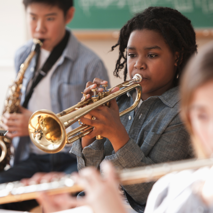 A young person plays a trumpet in a music class.