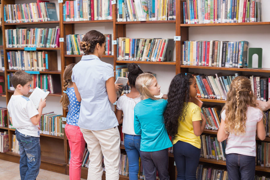 A group of children and an adult browse books in a library.
