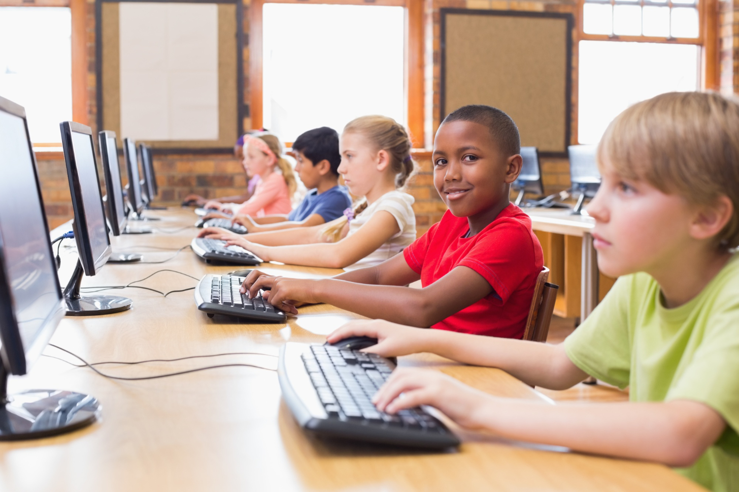 Children sit at computers in a classroom, focused on their screens.